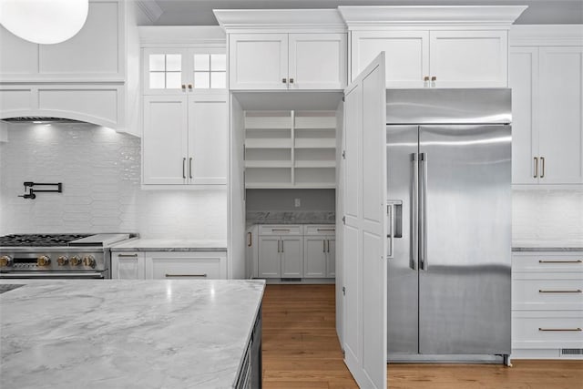 kitchen with premium appliances, white cabinets, wood-type flooring, backsplash, and light stone counters