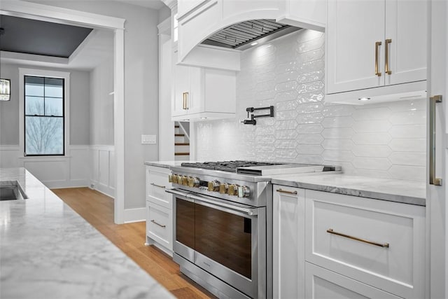 kitchen featuring white cabinetry, decorative backsplash, high end stainless steel range, and light stone countertops