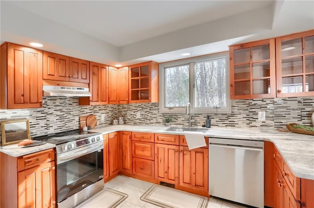 kitchen featuring tasteful backsplash, light stone countertops, appliances with stainless steel finishes, and sink