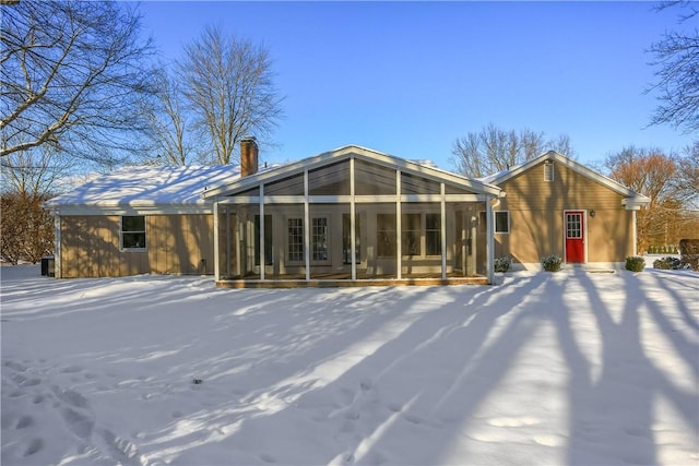 snow covered back of property featuring a sunroom