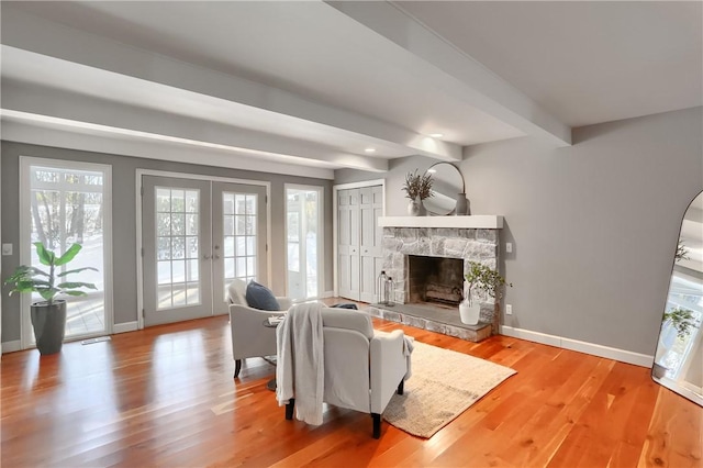 living room with light hardwood / wood-style flooring, french doors, a stone fireplace, and beamed ceiling