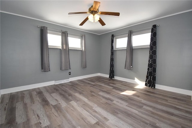 empty room with ceiling fan, a wealth of natural light, crown molding, and hardwood / wood-style flooring