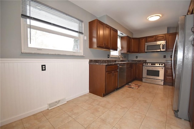 kitchen with light tile patterned floors, sink, dark stone countertops, and stainless steel appliances