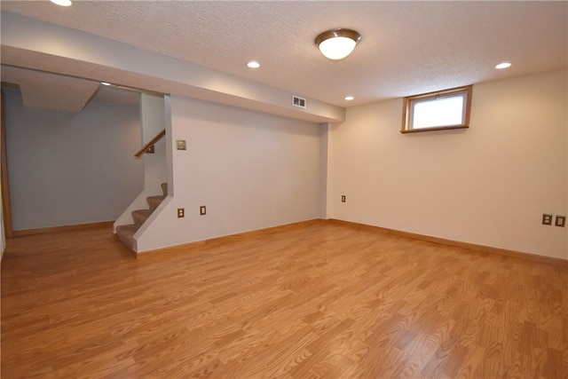 basement featuring a textured ceiling and light hardwood / wood-style floors