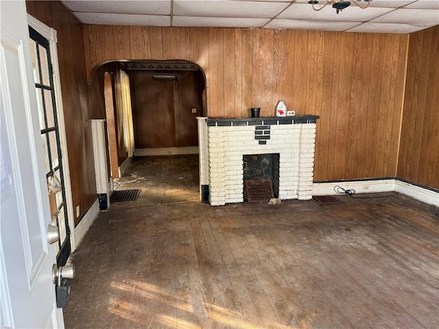 unfurnished living room with wood walls, a fireplace, and a drop ceiling