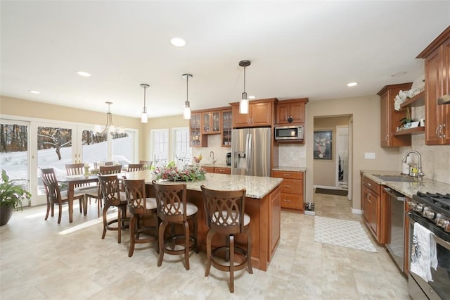 kitchen featuring sink, light stone counters, hanging light fixtures, a kitchen island, and stainless steel appliances