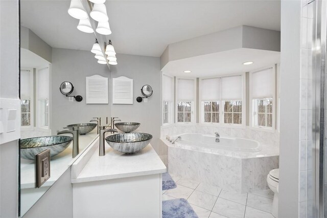 bathroom with a notable chandelier, vanity, toilet, and tiled tub