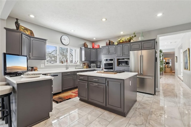 kitchen featuring appliances with stainless steel finishes, a kitchen island, sink, gray cabinetry, and a breakfast bar area