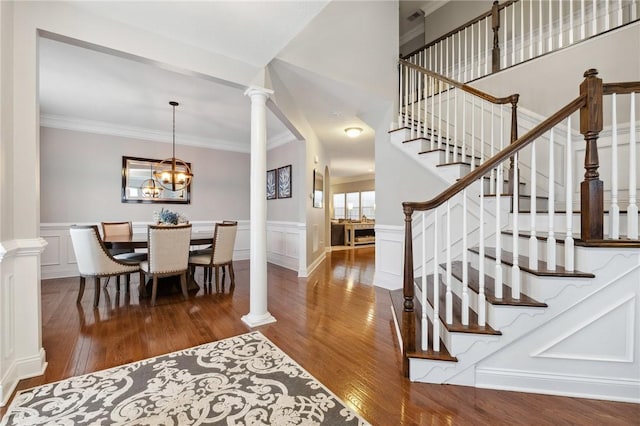 entryway featuring ornamental molding, dark hardwood / wood-style flooring, decorative columns, and a notable chandelier