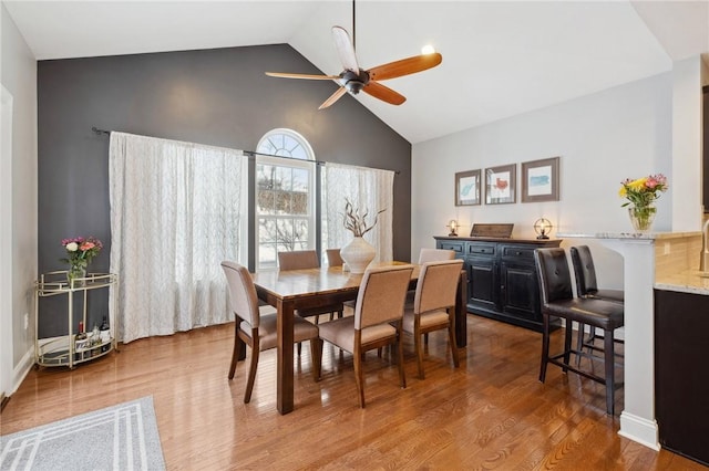 dining space with wood-type flooring, ceiling fan, and high vaulted ceiling