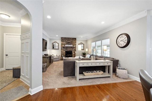 living room with a stone fireplace, ornamental molding, and hardwood / wood-style flooring