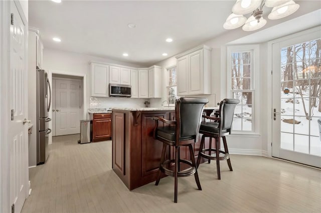 kitchen with white cabinets, a kitchen bar, stainless steel appliances, decorative backsplash, and light stone counters