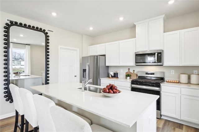 kitchen featuring white cabinetry, stainless steel appliances, and a center island with sink