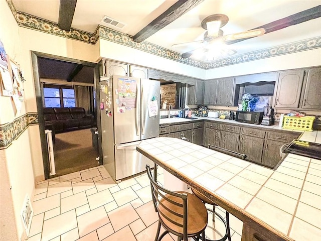 kitchen with dark brown cabinetry, stainless steel refrigerator, tile countertops, and light tile patterned flooring