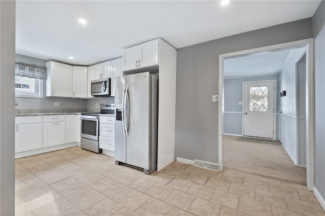 kitchen with stainless steel appliances, light colored carpet, white cabinetry, and light stone counters