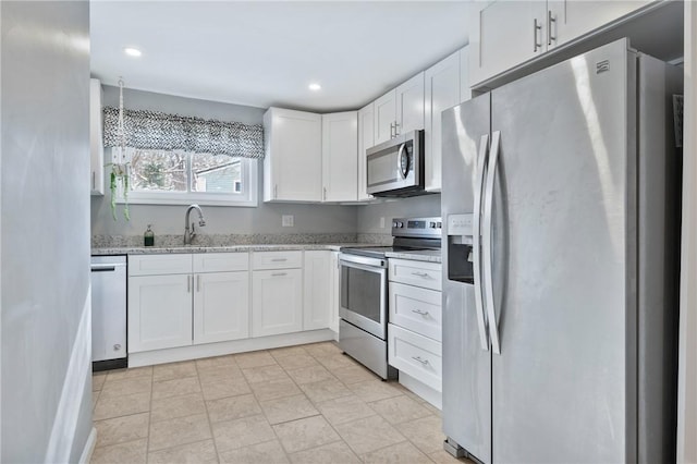 kitchen with appliances with stainless steel finishes, white cabinetry, light stone counters, and sink