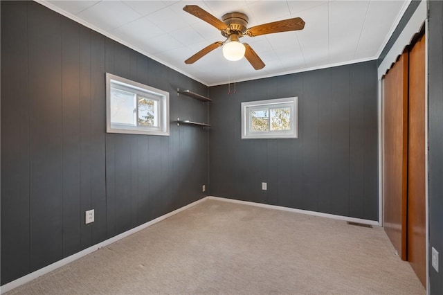 carpeted empty room featuring ceiling fan, ornamental molding, and a healthy amount of sunlight