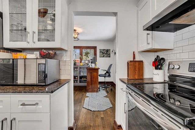 kitchen with stainless steel appliances, white cabinetry, dark stone counters, and wall chimney range hood