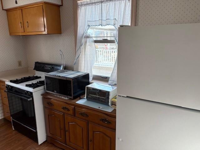 kitchen with hardwood / wood-style floors, range with gas stovetop, and white fridge