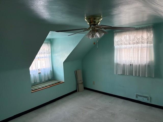 additional living space with ceiling fan, a wealth of natural light, light carpet, and vaulted ceiling