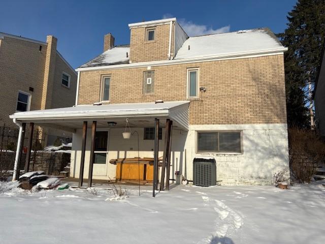 snow covered property with central AC unit and a hot tub