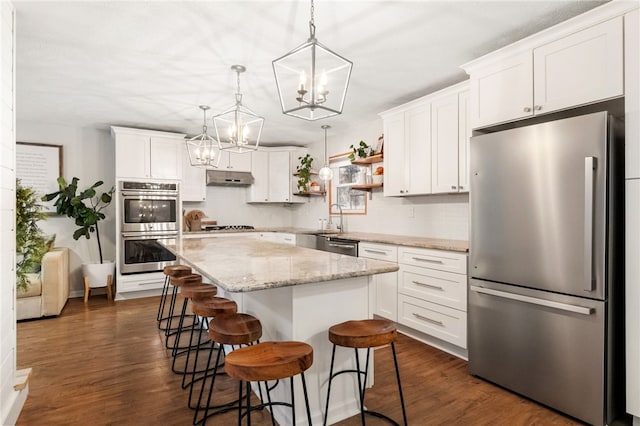 kitchen featuring white cabinets, appliances with stainless steel finishes, a center island, decorative light fixtures, and decorative backsplash