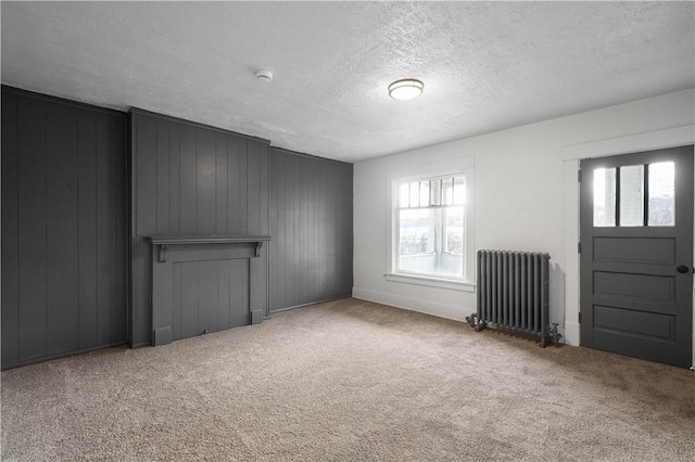 unfurnished living room featuring carpet floors, radiator, and wooden walls