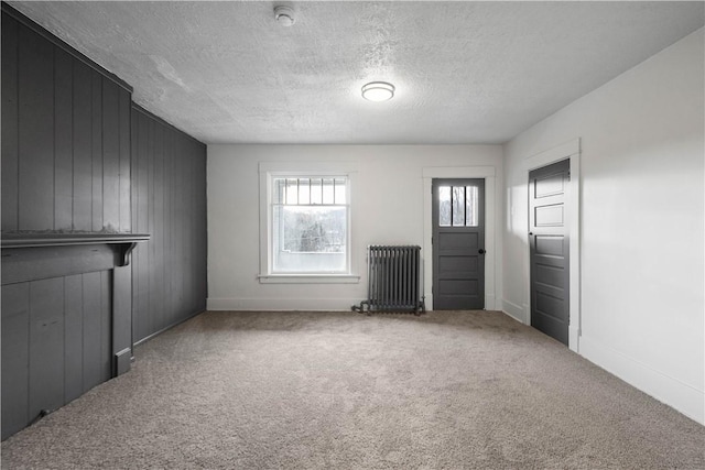 empty room with a textured ceiling, carpet, wooden walls, and radiator heating unit