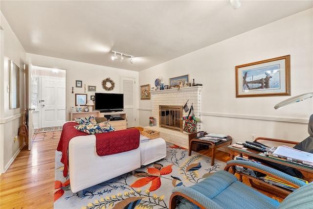 living room with light hardwood / wood-style floors, track lighting, and a brick fireplace