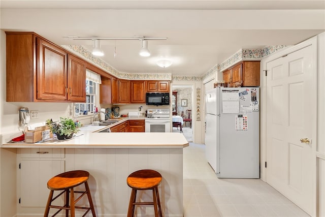 kitchen featuring kitchen peninsula, decorative light fixtures, a kitchen breakfast bar, white appliances, and sink