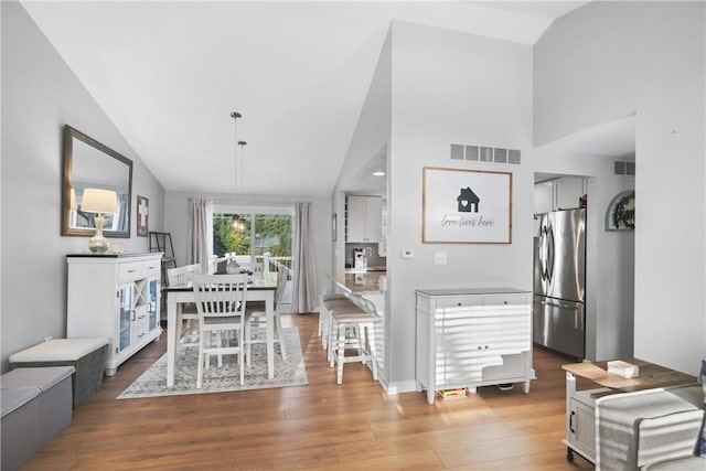 interior space with pendant lighting, light hardwood / wood-style floors, a breakfast bar, high vaulted ceiling, and stainless steel fridge