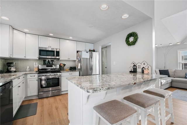 kitchen featuring light stone countertops, white cabinets, a kitchen bar, stainless steel appliances, and tasteful backsplash