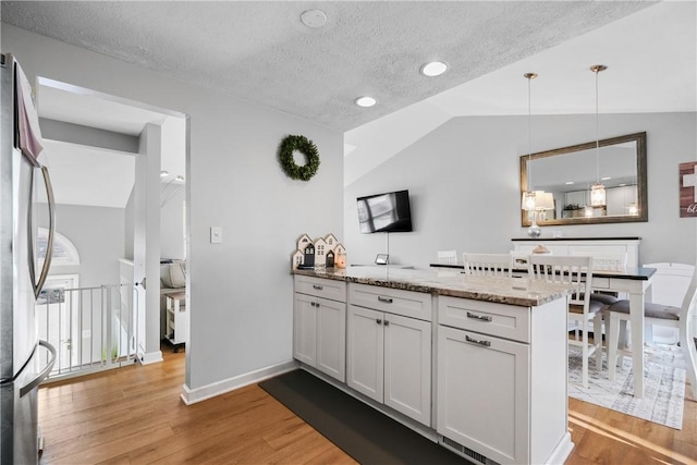 kitchen featuring a textured ceiling, lofted ceiling, white cabinetry, hanging light fixtures, and kitchen peninsula