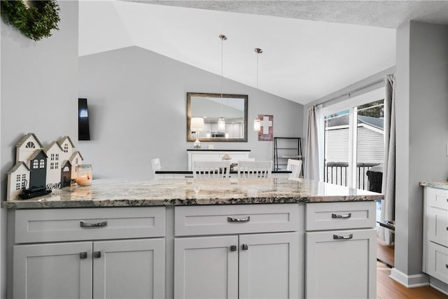 kitchen featuring lofted ceiling, light stone countertops, hanging light fixtures, and light hardwood / wood-style floors