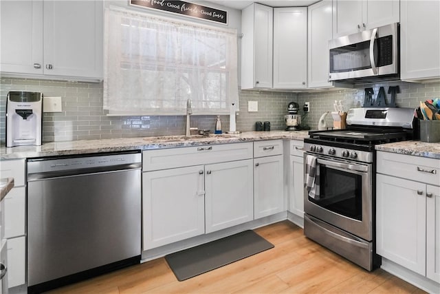 kitchen with light stone countertops, stainless steel appliances, white cabinets, and sink