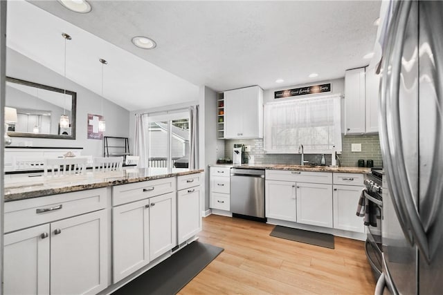 kitchen featuring white cabinetry, appliances with stainless steel finishes, hanging light fixtures, vaulted ceiling, and light stone counters