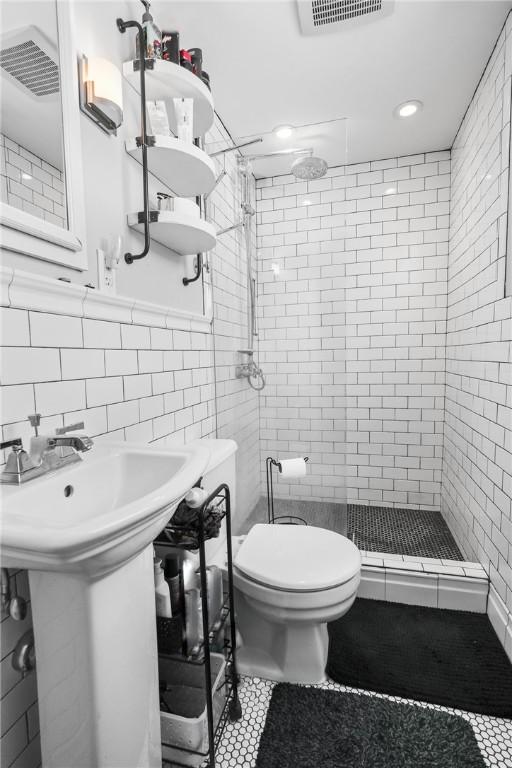 bathroom featuring toilet, tile walls, backsplash, and tiled shower