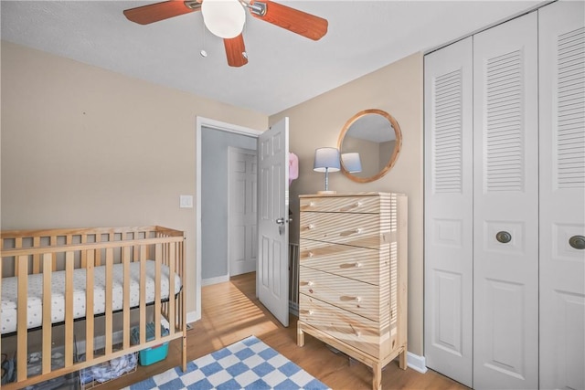 bedroom with ceiling fan, a closet, a crib, and light hardwood / wood-style floors