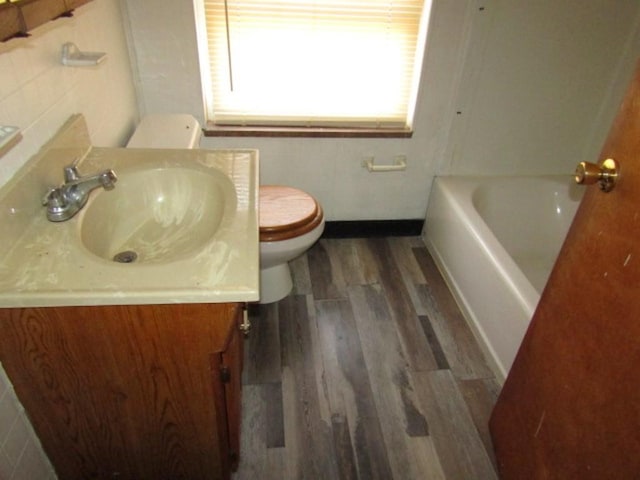 bathroom with hardwood / wood-style floors, toilet, vanity, and a tub to relax in