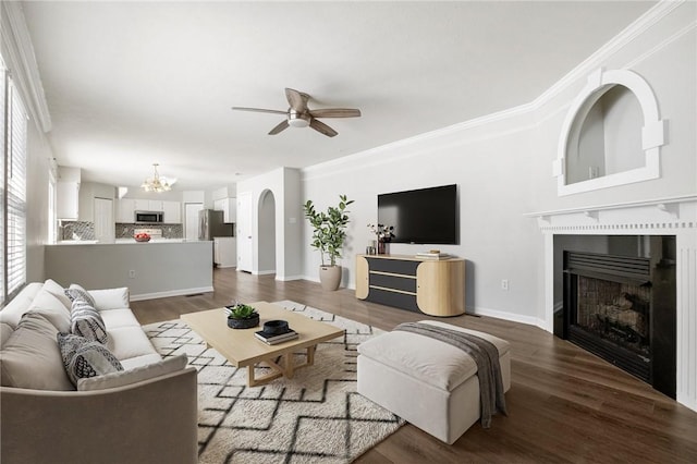 living room featuring dark wood-type flooring, ornamental molding, and ceiling fan with notable chandelier