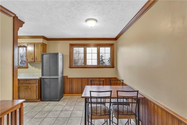 kitchen featuring a textured ceiling, light tile patterned floors, crown molding, and wooden walls