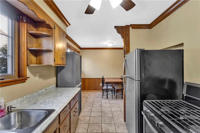 kitchen featuring sink, wooden walls, crown molding, light tile patterned flooring, and appliances with stainless steel finishes