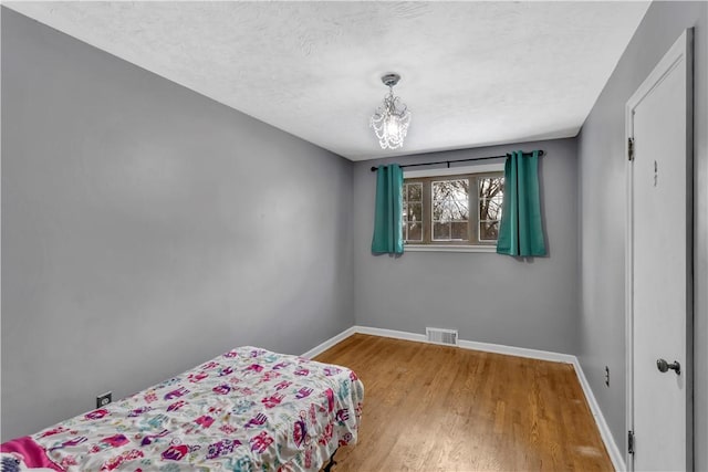 bedroom featuring wood-type flooring, a textured ceiling, and a notable chandelier