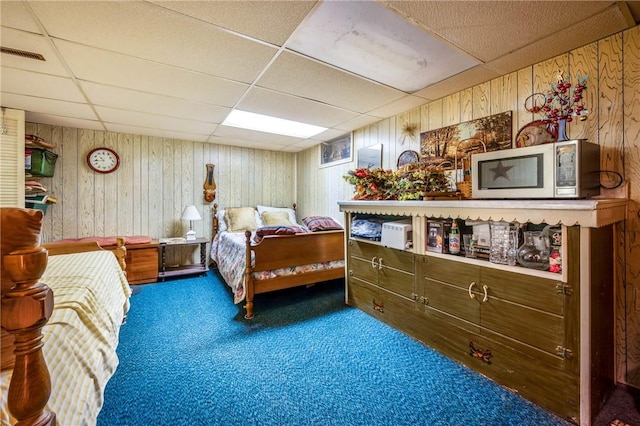 carpeted bedroom with a drop ceiling and wood walls