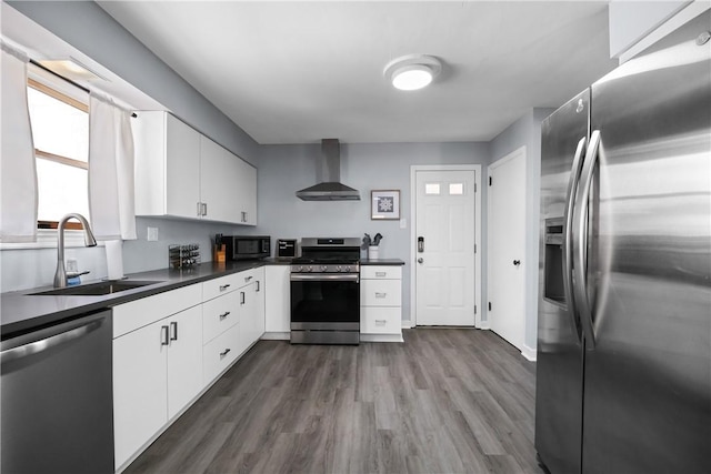 kitchen featuring appliances with stainless steel finishes, sink, wall chimney range hood, dark wood-type flooring, and white cabinets