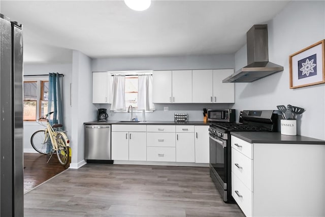 kitchen with appliances with stainless steel finishes, sink, wall chimney range hood, white cabinets, and hardwood / wood-style flooring