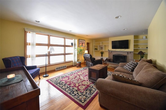 living room featuring light wood-type flooring, a brick fireplace, and built in shelves