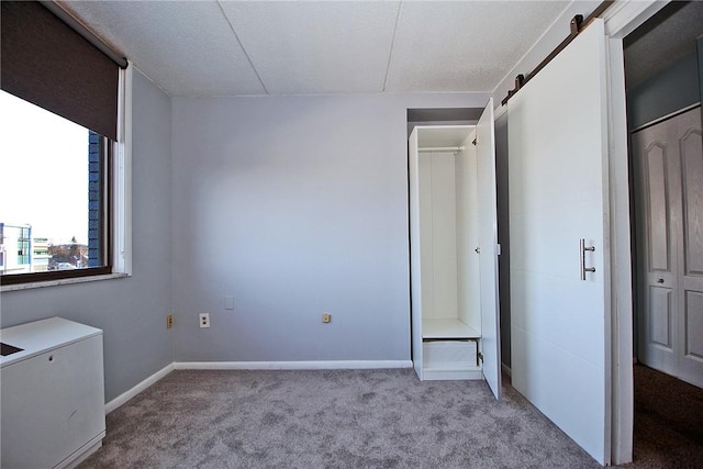 unfurnished bedroom with light carpet, a barn door, and a textured ceiling