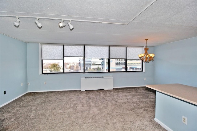 carpeted empty room featuring a healthy amount of sunlight, track lighting, radiator heating unit, and a chandelier