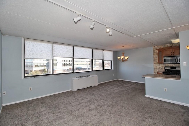 interior space featuring a chandelier, hanging light fixtures, radiator, stainless steel appliances, and dark carpet